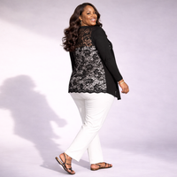 Woman wearing a black lace top and white pants on a plain background