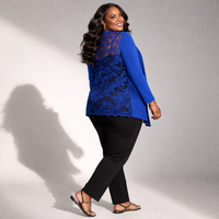 Woman wearing a blue lace top and black pants against a gray background