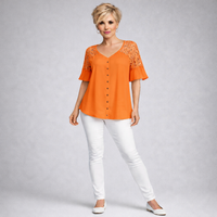 Woman wearing an orange blouse with lace details and white pants on a gray background