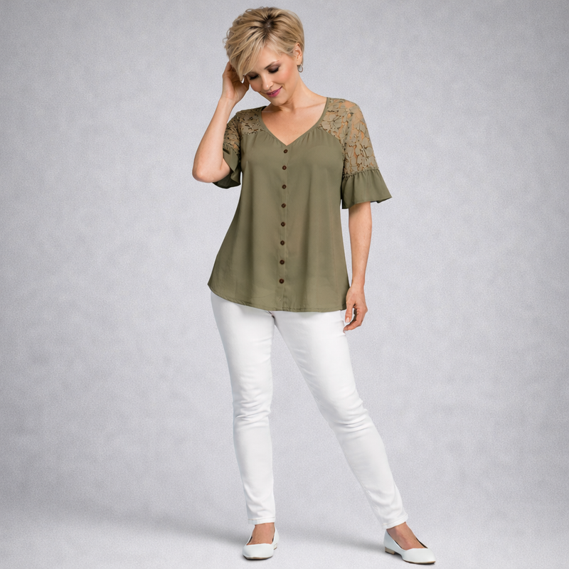 Woman wearing an olive green blouse with lace sleeves and white pants on a gray background