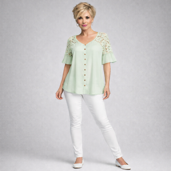 Woman wearing a light green blouse with lace sleeves and white pants on a gray background