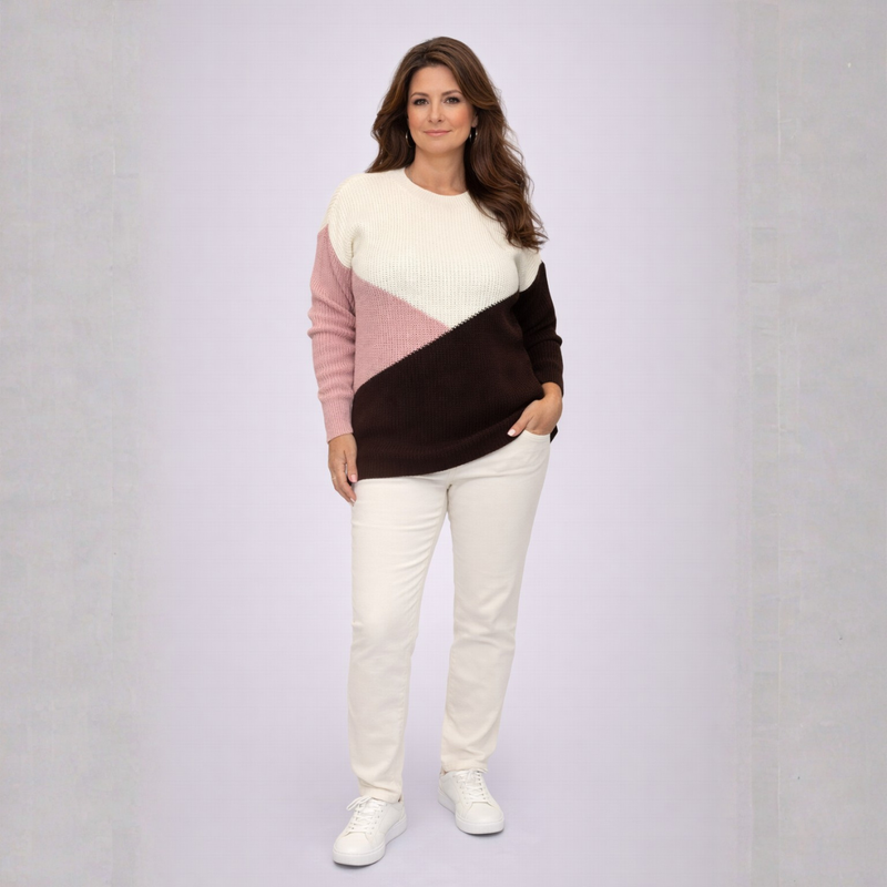 Woman wearing a color-blocked sweater and white pants on a plain background